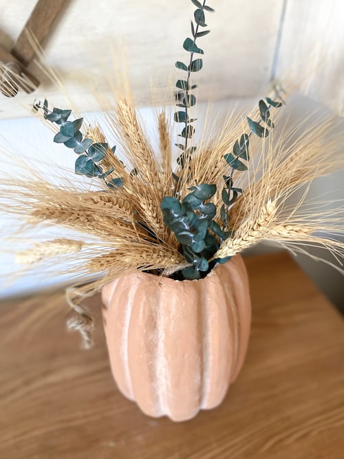 This DIY Fall Centerpiece gives the look of a terra cotta pumpkin vase for a lot less by using paper mache, paint, and baking soda!