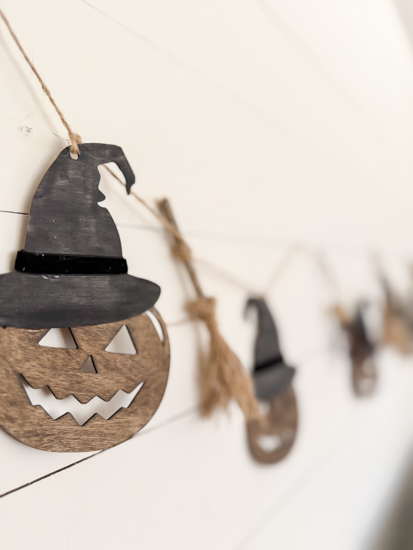 Make this DIY Rustic Halloween Garland with Dollar Tree wood cutouts, stain, witch hats, velvet ribbon, twine, and mini witch brooms.
